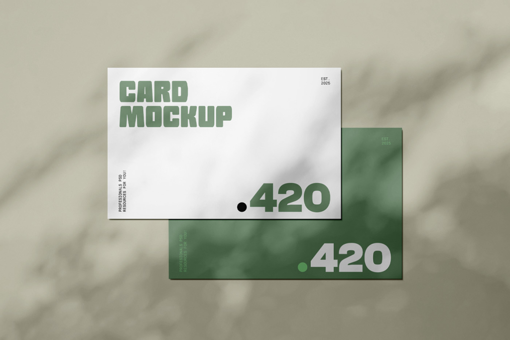 Top-down photograph of two overlapping, blank white rectangular cards, used as an envelope mockup, resting on a light grey background. The scene is cast with a soft, dappled shadow pattern from above, resembling the effect of light passing through foliage. Free Lying Postcard Mockups