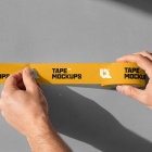 Close-up of hands sticking a strip of yellow printed tape onto a smooth grey wall.