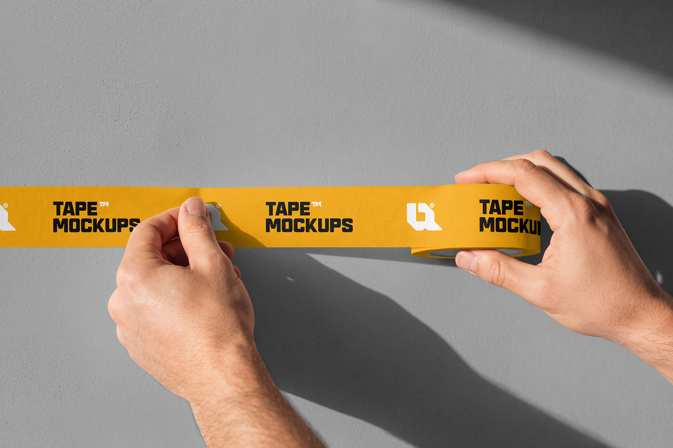 Paper-Tape-Mockup-01-CRM-a Close-up of hands sticking a strip of yellow printed tape onto a smooth grey wall.