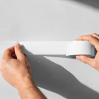 Close-up of hands applying a strip of white masking tape onto a light-colored wall.