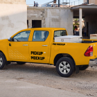 Side view of a yellow crew-cab pickup truck with custom branding parked at an active construction site.