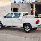 Side view of a white pickup truck with a silver toolbox in the bed parked at a construction site.