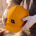 Close-up of a construction worker wearing protective gloves holding a yellow hard hat.