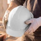 Close-up of a construction worker wearing protective gloves holding a white safety hard hat.