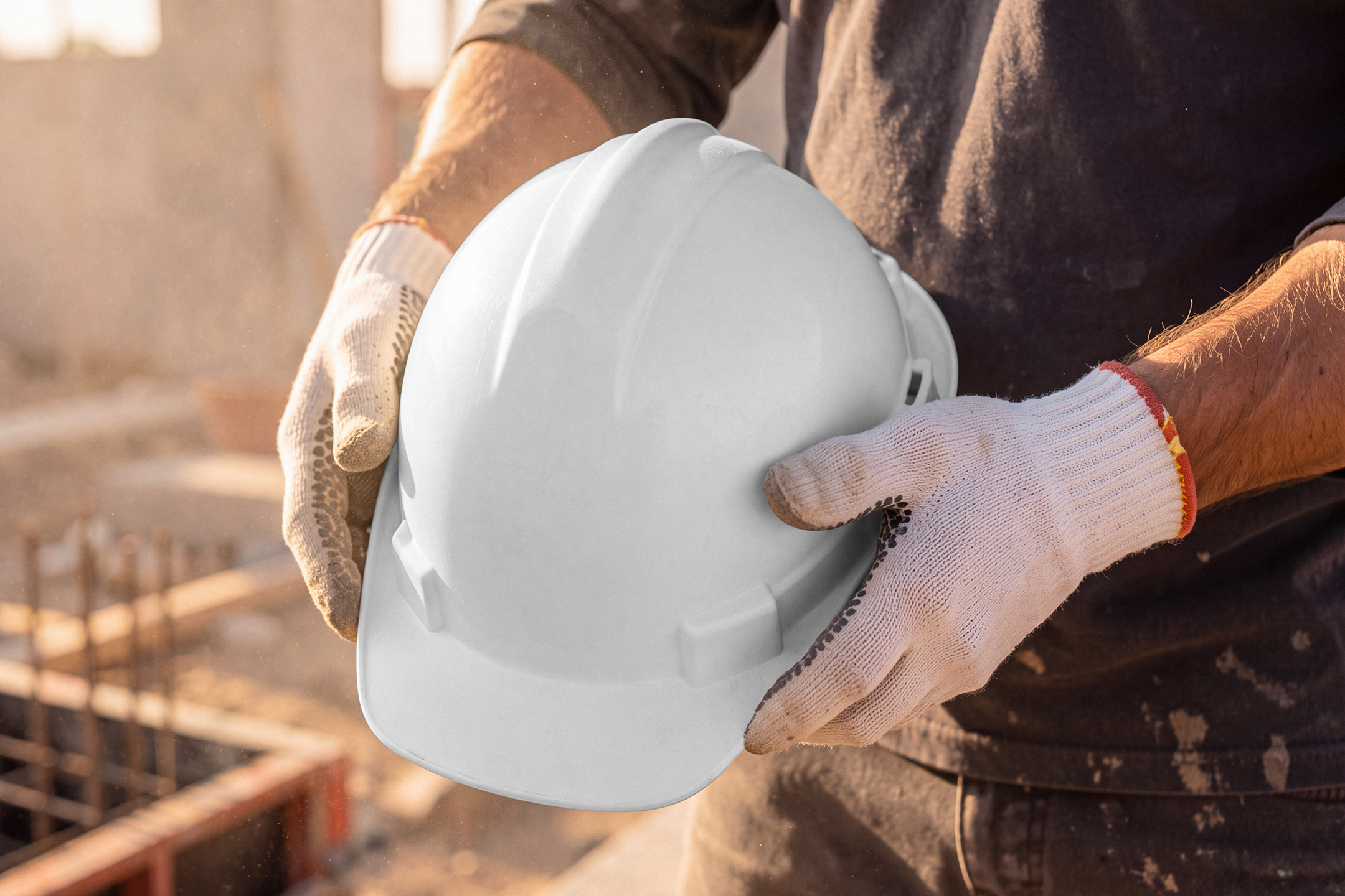 Close-up of a construction worker wearing protective gloves holding a white safety hard hat.