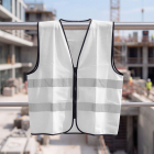 A white high-visibility safety vest is hanging on a metal railing at a blurred construction site.