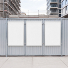 Three blank white vertical poster mockups mounted on a corrugated metal fence at a building site.