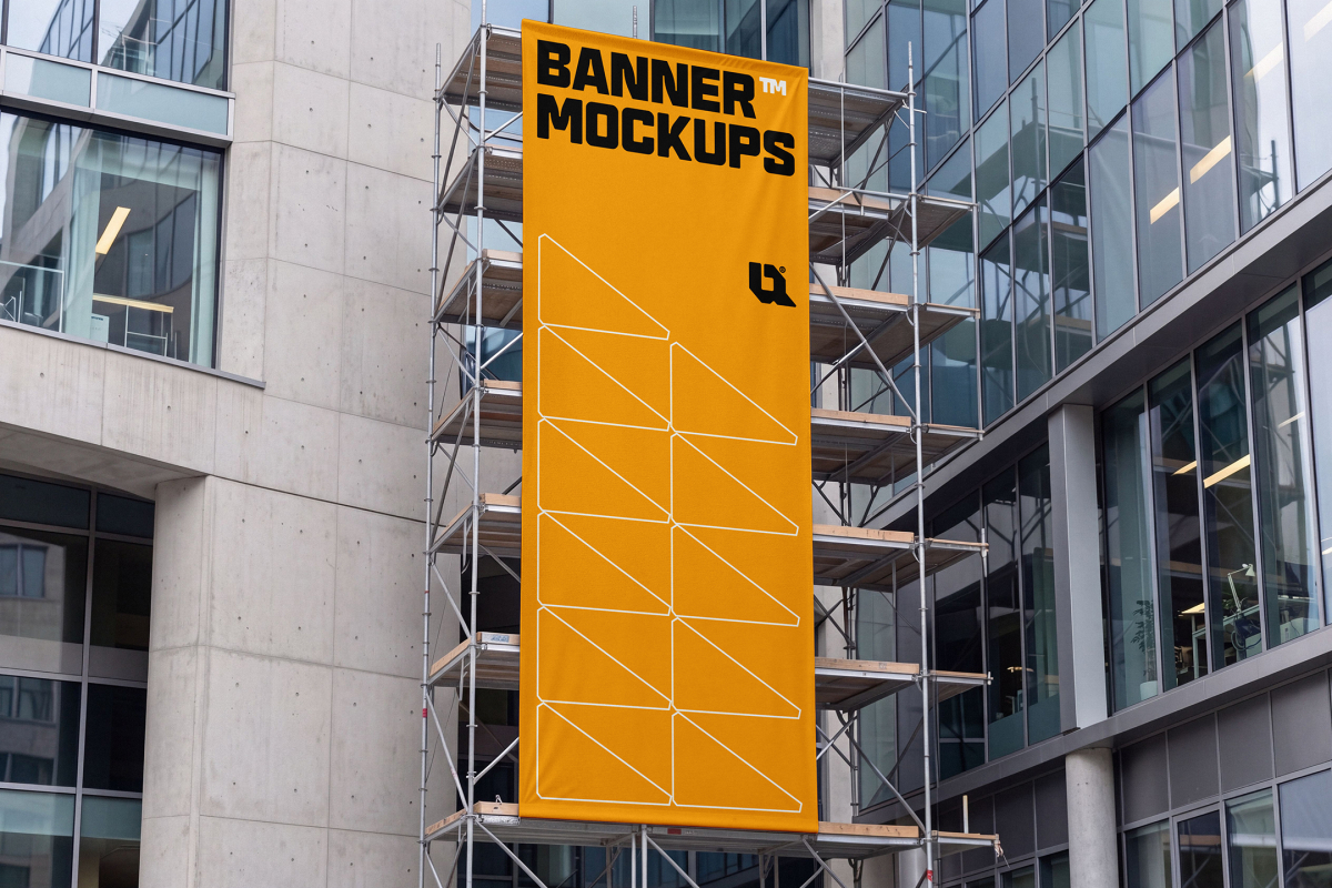 A tall vertical yellow banner is displayed on metal scaffolding against a modern glass building facade.