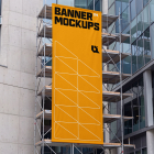 A tall vertical yellow banner is displayed on metal scaffolding against a modern glass building facade.