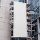 Large blank white vertical banner displayed on scaffolding outside a modern glass office building.