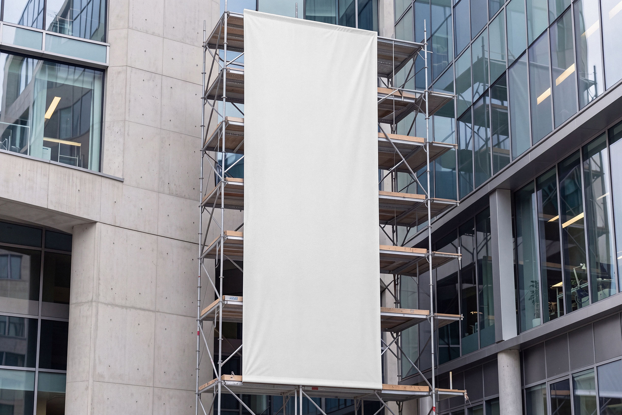Large blank white vertical banner displayed on scaffolding outside a modern glass office building.